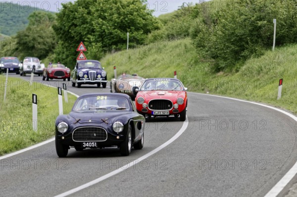 Black classic car followed by red and other classic cars on a winding road, dynamic race, classic