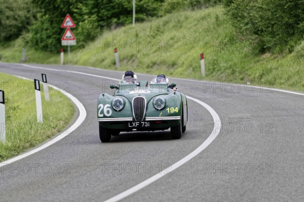 Two people in a green vintage convertible with racing numbers, fast drive on country road, vintage