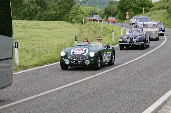 Green classic car in a row of vehicles on a winding country road, classic car, car race, Mille
