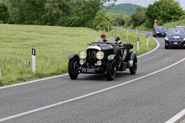 A classic vintage car with two drivers takes part in a car rally on a picturesque road, classic