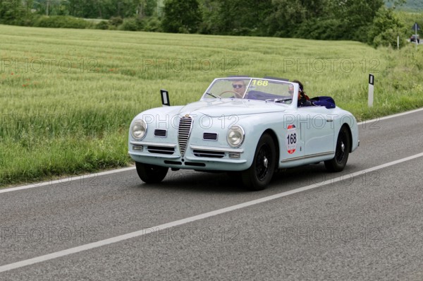 Blue convertible on a country road with green meadows in the background, classic car, car race,