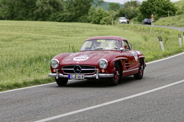 A red Mercedes classic car drives along a picturesque country road surrounded by trees, classic