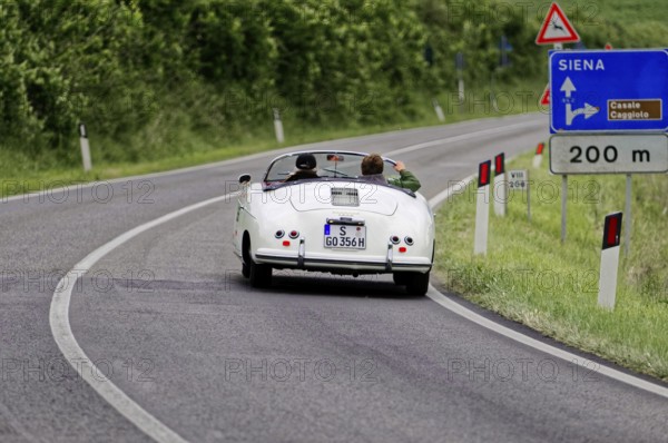 A white vintage convertible on an open country road towards Siena, vintage car, car race, Mille