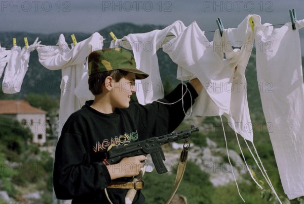 HRV, Kraotien, Dubrovnik 20.09.1993 Child with toy gun behind laundry. HRV Croatia, Dubrovnik, 1993