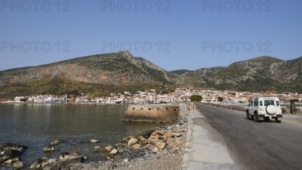 An off-road vehicle on a coastal road with a view of a city and mountains, Monemvasia, Monemvassia,