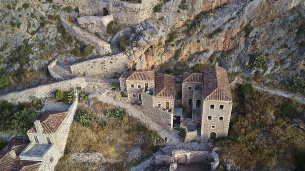 Drone view, aerial view of an ancient fortress with stone houses and vegetation on rocky terrain,