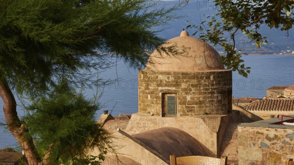 Soft morning light, view over a dome and the sea, framed by green trees and tiled roofs,