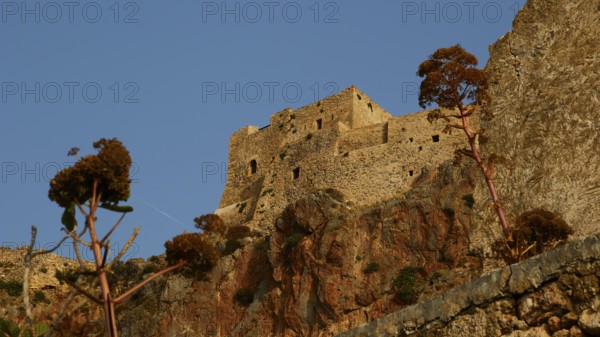 Soft morning light, old stone fortress on rocks with plants, under clear sky, Monemvasia,