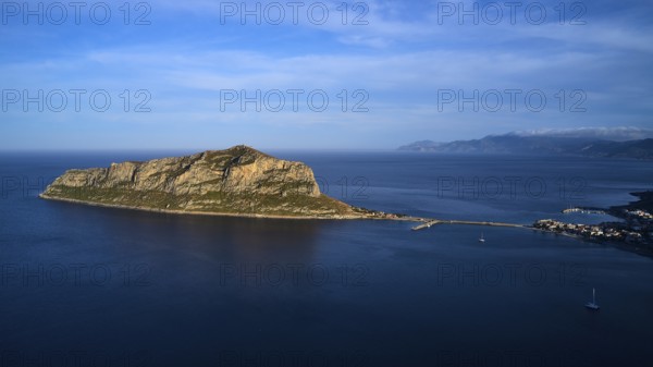 Drone shot, island in the sea, connected by bridge, mountains and sky in the background,