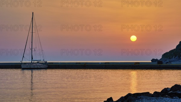 Sailing boat against orange sky and calm sea at sunrise, Monemvasia, Monemvassia, Malvasy,