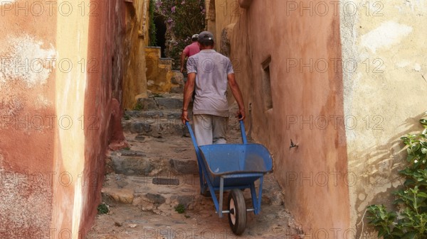 A man pulls a wheelbarrow up a narrow, colorful alley, Monemvassia, Malvasy, small Byzantine town,