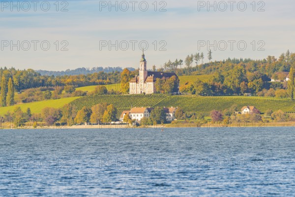 A church on a hill above autumn vineyards and a lake, surrounded by picturesque landscapes and