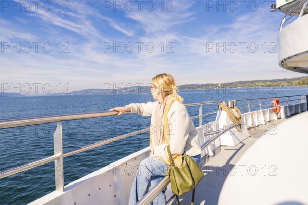 A woman stands relaxed at the railing of a ship and looks out to sea in sunny weather, Schiff