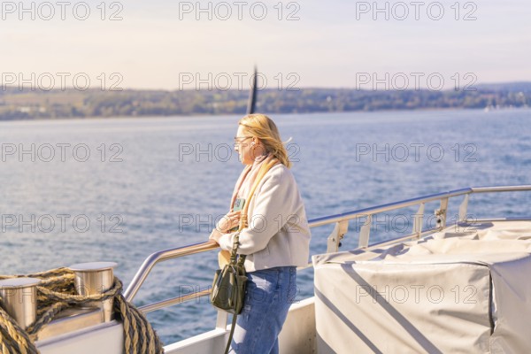 Woman leaning calmly on the railing with a view of the vast water landscape, boat trip, Lake
