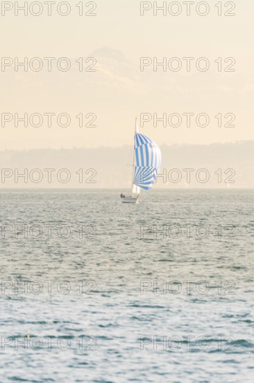 Sailing boat with blue and white sail floating on a wide lake against a mountain backdrop, Schiff
