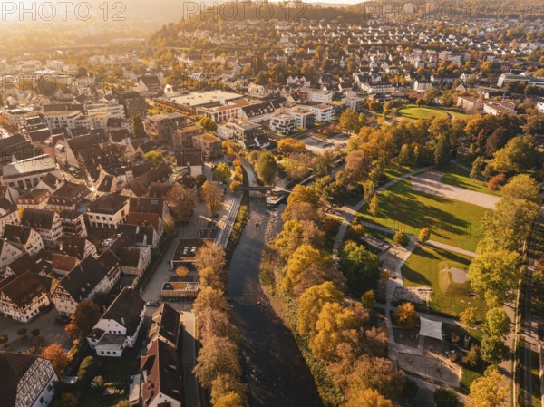 An autumnal view of the city with a river and lots of colorful trees illuminated by the sun,