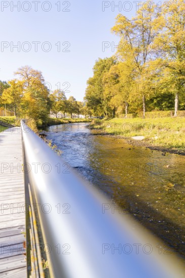 A river flows under a bridge, surrounded by autumn-colored trees on a sunny day, Nagold, Black