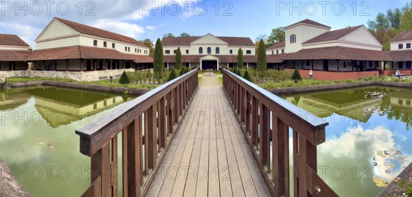 View from site of archaeological open-air museum across small wooden bridge across ornamental pond