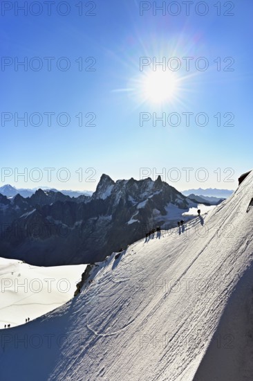 Mountaineers climb over a snow-covered ridge, behind Grandes Jorasses, Aiguille du Midi mountain