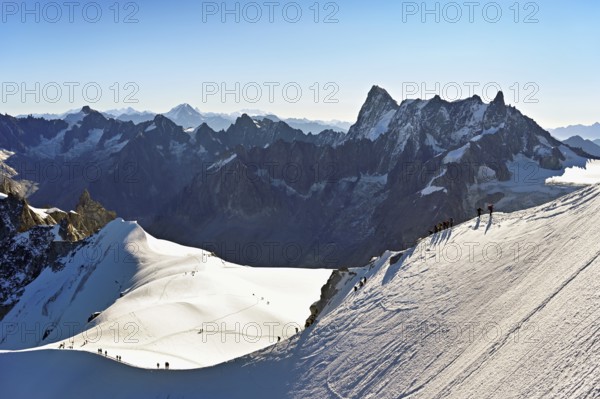 Mountaineers climb over a snow-covered mountain ridge, behind Grandes Jorasses, viewing platform,