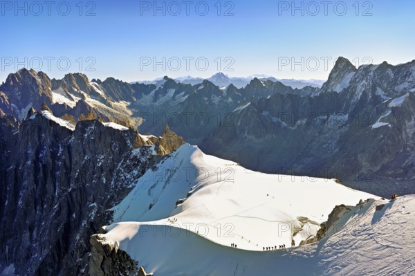 Mountaineers climb over a snow-covered ridge, behind Aiguille Verte, Les Droites, Les Courtes,