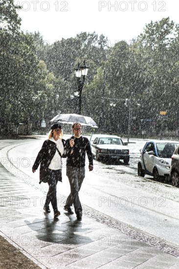 DEU Germany Germany Berlin A couple walking with an umbrella through a summer rain shower at the