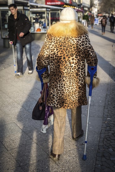 DEU Germany Germany Berlin A woman wears a leopard cloak while using crutches on the Kudamm to pass