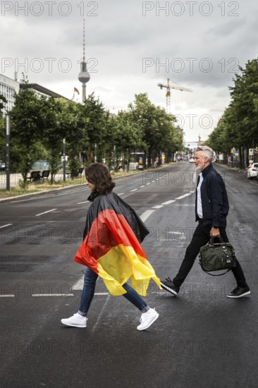 DEU Germany Germany Berlin Tourist with rain capes in the colours of Germany crosses a pedestrian