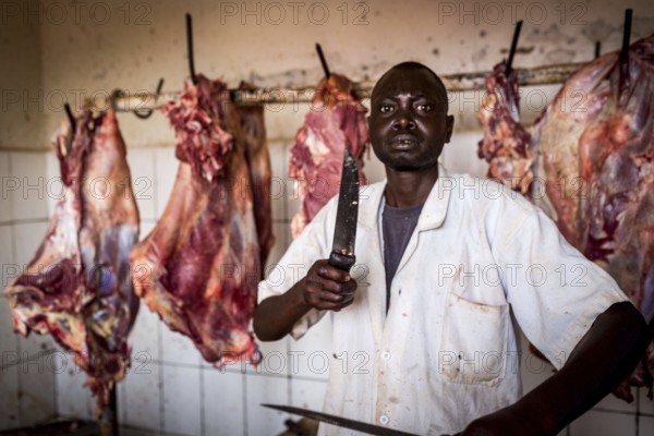 RWA RWANDA Rwanda Kayonza A butcher sharpens his knives in front of pieces of meat. He poses for