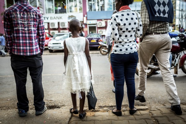 RWA RWANDA RUANDA Kigali A young girl with a white dress and handbag waits with others until she