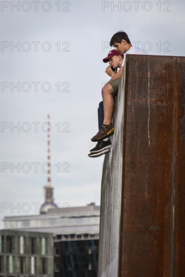 DEU Germany Germany Berlin In summer temperatures, two young people sit on a wall on the Spreebogen