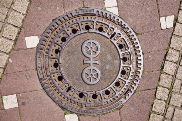 Manhole cover, city coat of arms, sidewalk made of concrete paving stones and paving stones with