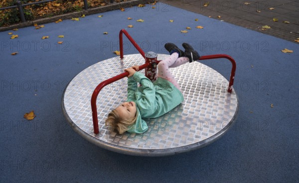 Outdoor shot, little girl, child, 4 years, blonde, playing on carousel, children's playground,