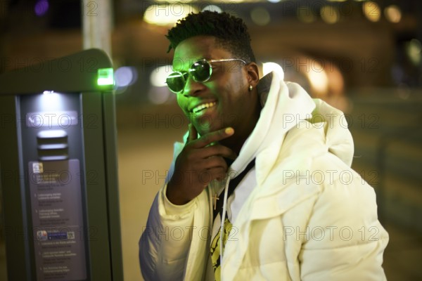 Thoughtful greenlit African man at parking ticket machine pausing as symbol for approved