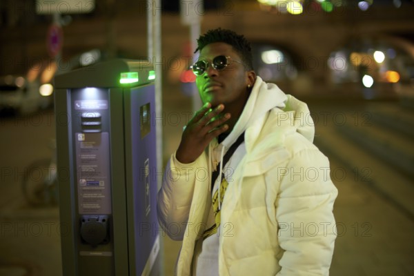Thoughtful greenlit African man at parking ticket machine pausing as symbol for approved