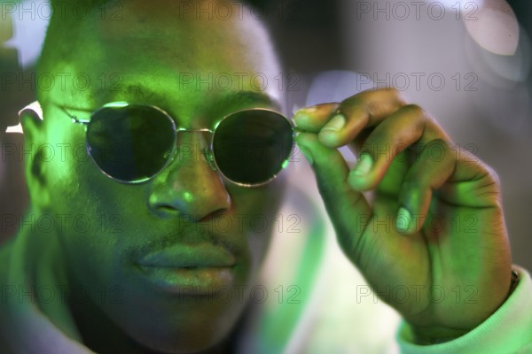 Greenlit African man wearing sunglasses at night as shade of anonymity, coolness, approved