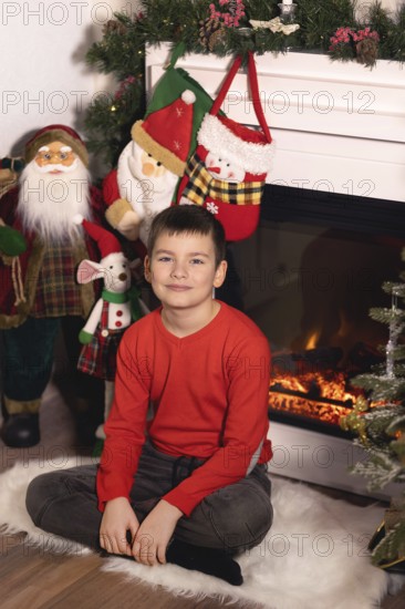 Young boy smiling, sitting on a rug with christmas decorations and a lit fireplace.Belarus