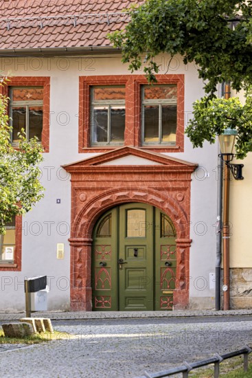 Historic building façade with green door and decorative red stone decorations, surrounded by trees