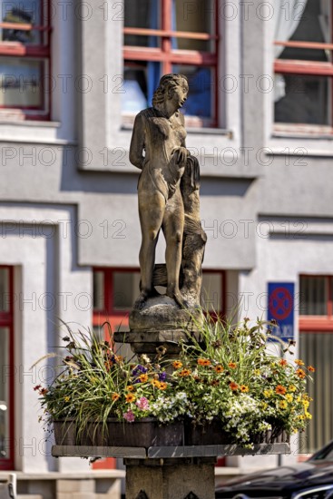 Stone figure on a fountain with surrounding flowers in front of a building, statue and monument in
