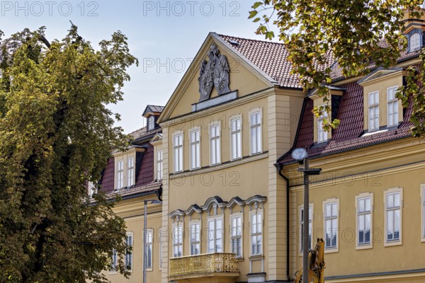 Historic baroque building with yellow façade, decorated gable, surrounded by trees, the façade of