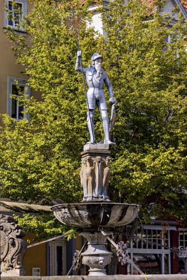 Metal statue of a warrior on a fountain surrounded by green trees, statue and monument in the old