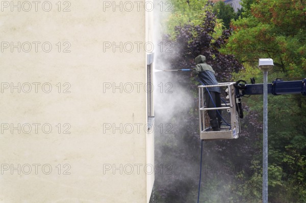 Unrecognizable man cleaning facade surface from lifting platform with high pressure stream of water