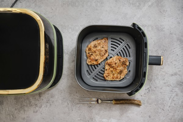 Two cooked seasoned pork sirloin cutlets in the basket of an air fryer. The kitchen setting