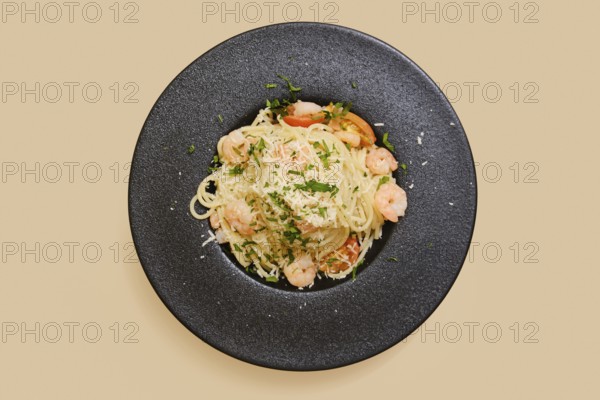 Delicious creamy garlic shrimp pasta in a black plate, garnished with herbs and cheese. This