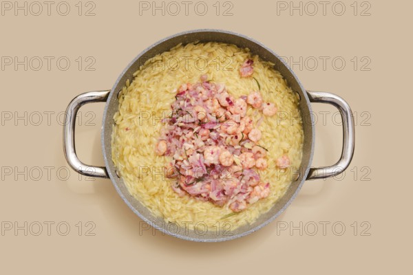 A pot with cooked risoni pasta and fresh shrimps. The dish features a creamy texture and vibrant