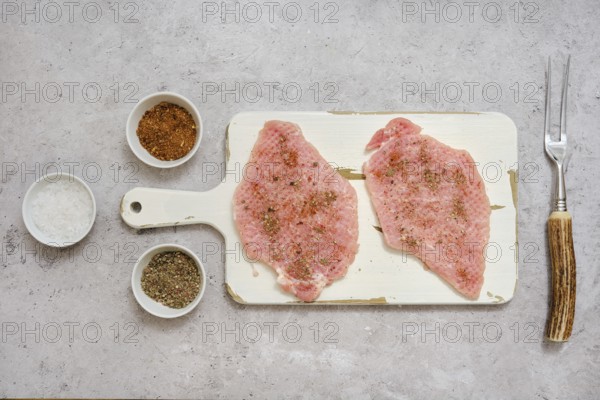 Two pork sirloin chops on a cutting board, seasoned with various spices, in a well-lit kitchen.