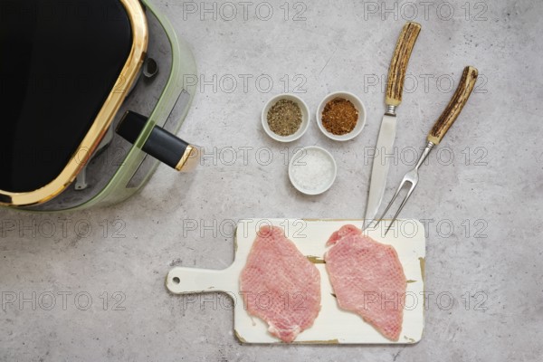 Two raw pork sirloin cutlets are placed on a cutting board next to small bowls filled with spices.