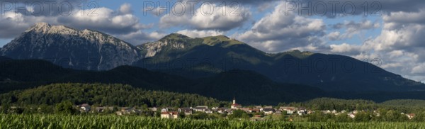 A Slovenian village is nestled between green fields and the imposing peaks of the Julian Alps near