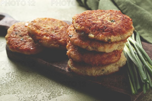 Crispy potato pancakes Latkes, stacked on a wooden board next to fresh green onions, natural light,
