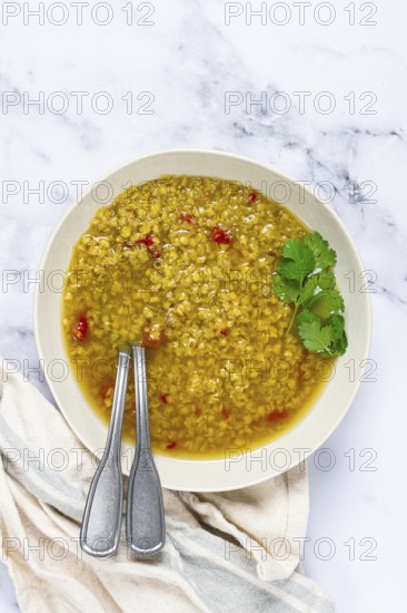 A warm bowl of lentil soup features a golden broth filled with spices and herbs. Fresh cilantro